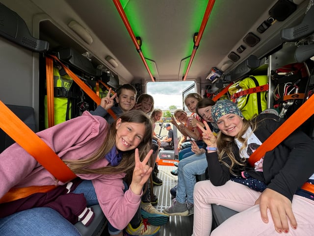 Kinder sitzen angeschnallt in der Mannschaftskabine eines Feuerwehrautos und lachen in die Kamera.